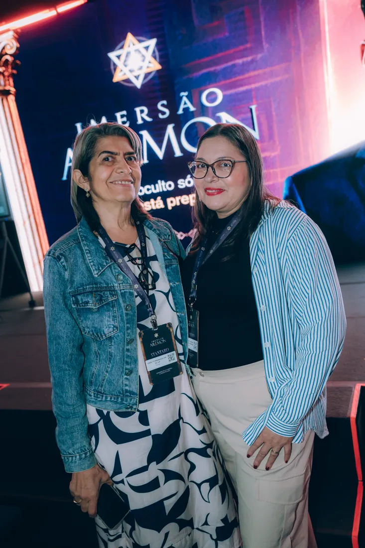Duas participantes sorrindo em frente ao painel do AREMON
